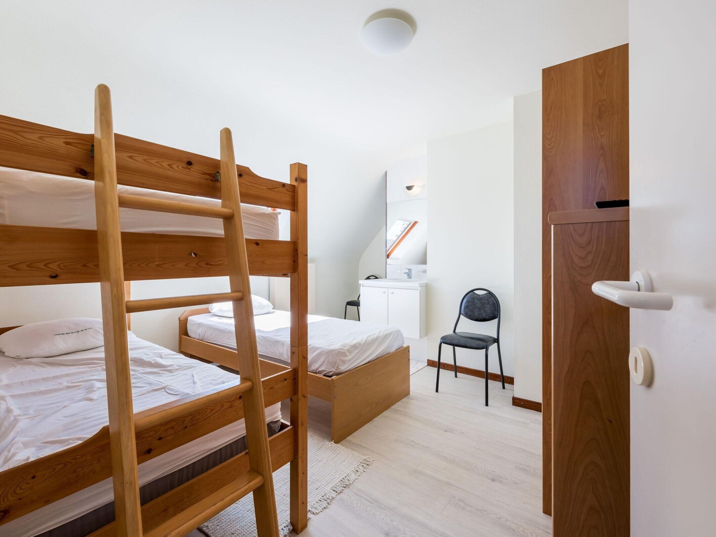 A bunk bed room with a wooden ladder, a desk with a chair, a mirror, and a wardrobe.