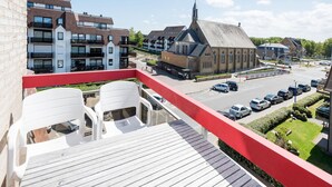 Ein Balkon mit weißen Plastikstühlen, Blick auf eine Kirche und ein Parkplatz mit Autos.
