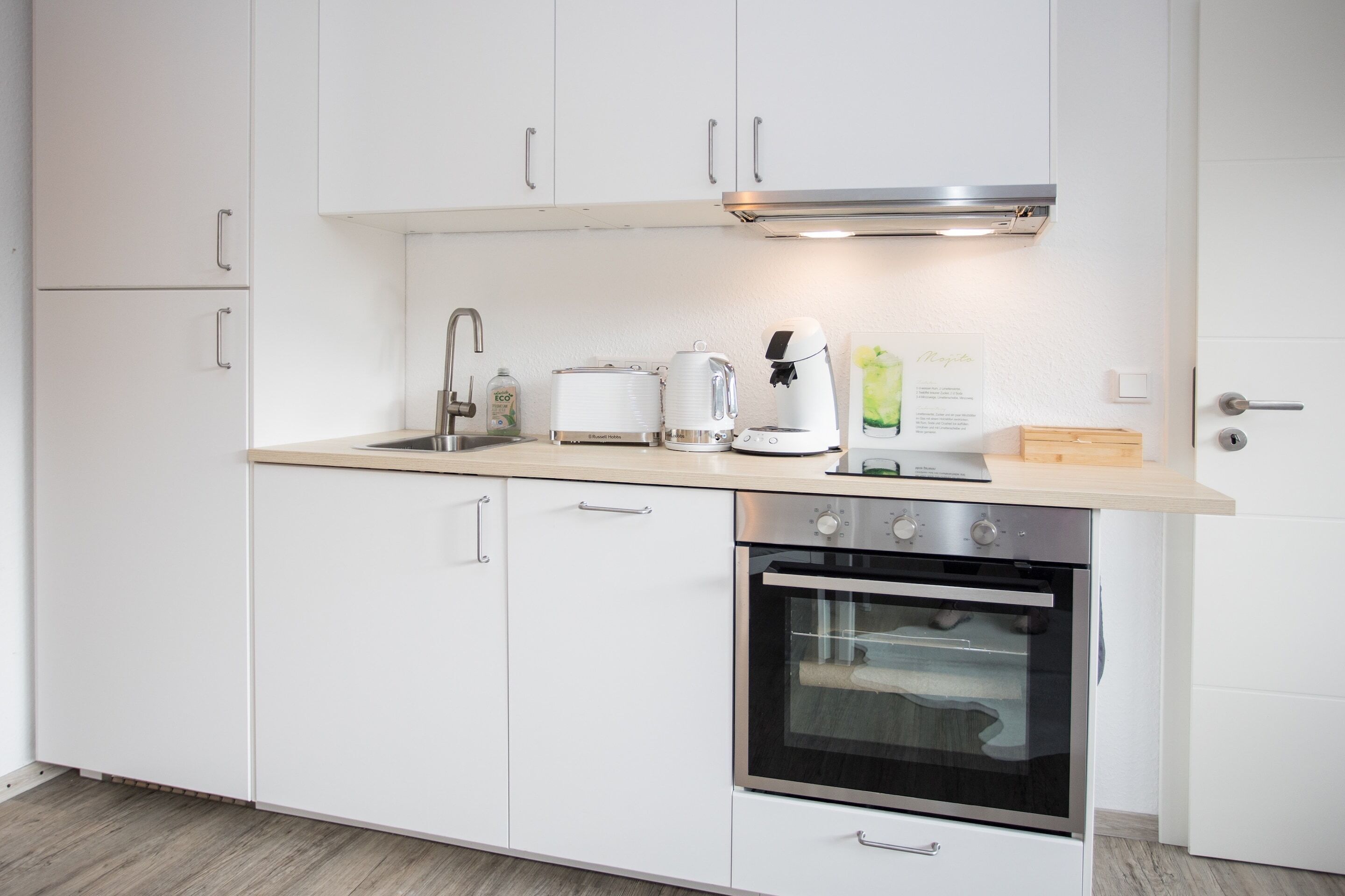 A modern kitchen with white cabinets, a stainless steel oven, a coffee maker, and a toaster.