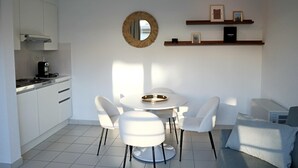 A modern kitchen with white cabinets, a round mirror, and a dining area with a white table and chairs. - Apartment in Nieuwpoort Near the Beach (Nieuwpoort)