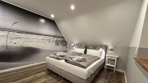 A bedroom with a bed, a nightstand, a wall mural, and a wooden floor. - Eiderhuus Modern Retreat (Toenning)
