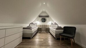A modern, minimalist attic bedroom with two beds, a round window, and a built-in wardrobe. - Eiderhuus Modern Retreat (Toenning)