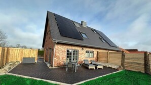 A house with a brick exterior, a sloped roof with solar panels, a covered patio with a table and chairs, and a fenced backyard. - Eiderhuus Modern Retreat (Toenning)