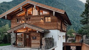 A two-story wooden chalet with a stone entrance and a mountain backdrop. - Chalet Alpin Comfortable Holiday Residence (Bayrischzell)