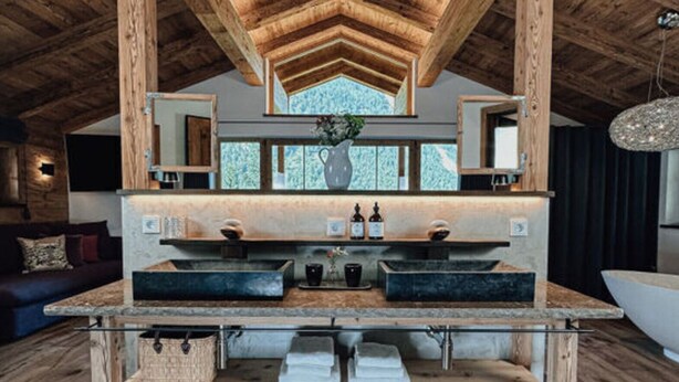 A rustic bathroom with wooden beams, a large mirror, and a window with a view. - Chalet Alpin Comfortable Holiday Residence (Bayrischzell)