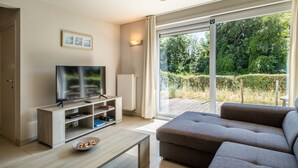 Ein modernes Wohnzimmer mit Fernseher, einer Couch und einem Esstisch.