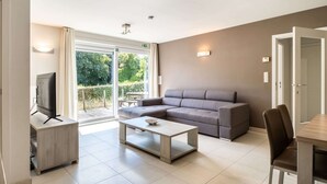 Ein modernes Wohnzimmer mit grauem Sofa, Couchtisch, Fernseher und Essbereich mit Stühlen.