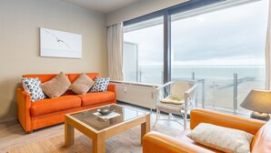 A modern living room with an orange sofa, a glass coffee table, and a wicker chair. - Apartment With a Beautiful Terrace and sea View (Middelkerke)