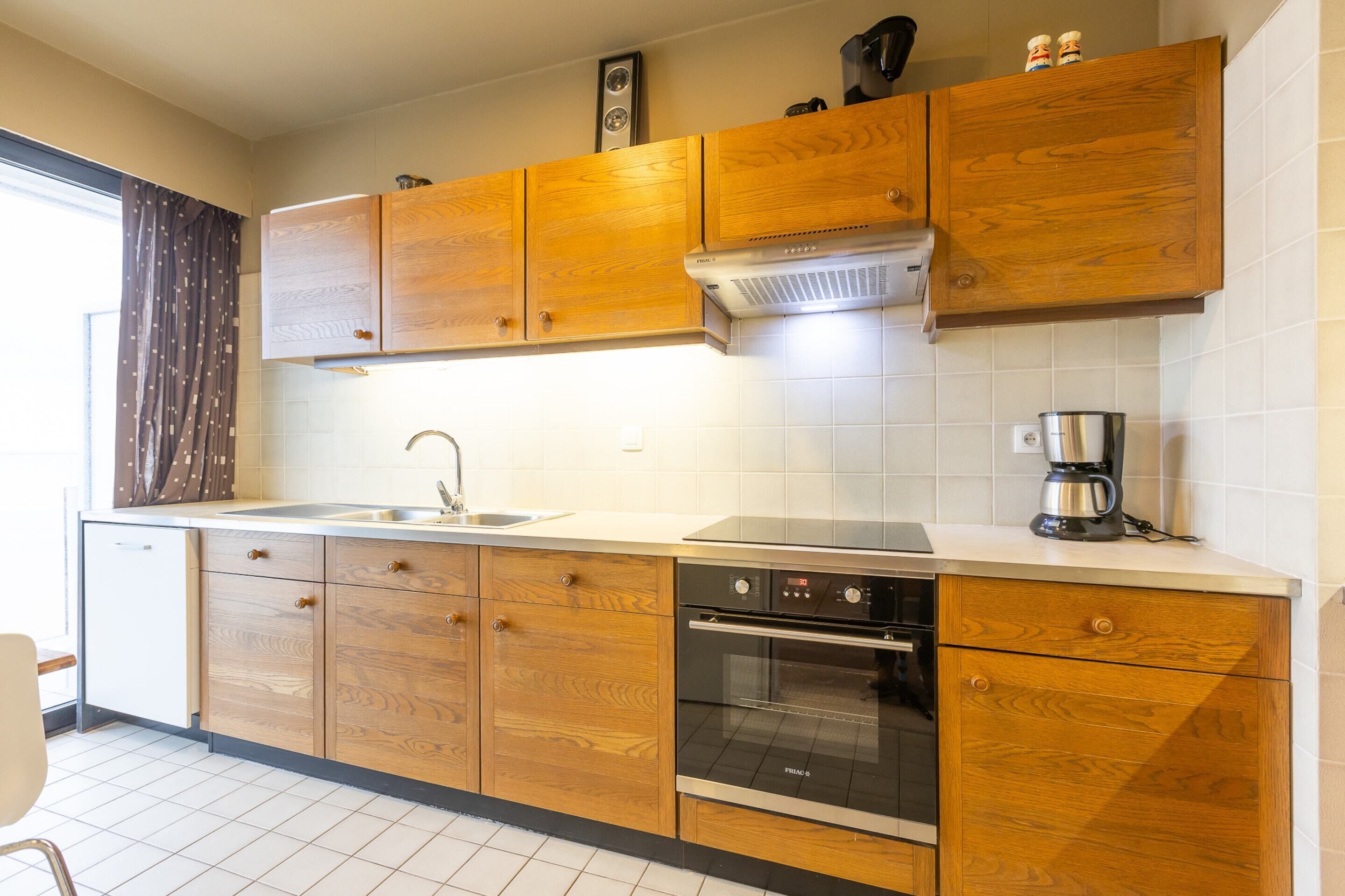 Une cuisine avec des meubles de rangement en bois, un évier en acier inoxydable, un four encastré et une machine à café.