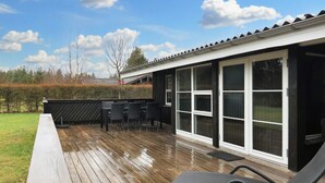 Une terrasse extérieure couverte, dotée d’une table et de chaises, une terrasse en bois et un bâtiment avec de grandes fenêtres.