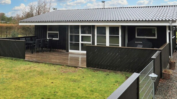 Une maison moderne dotée d’un patio couvert, de grandes fenêtres et d’un espace barbecue.