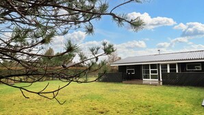 Un bâtiment doté d’un patio couvert, entouré d’un champ verdoyant et d’arbres.