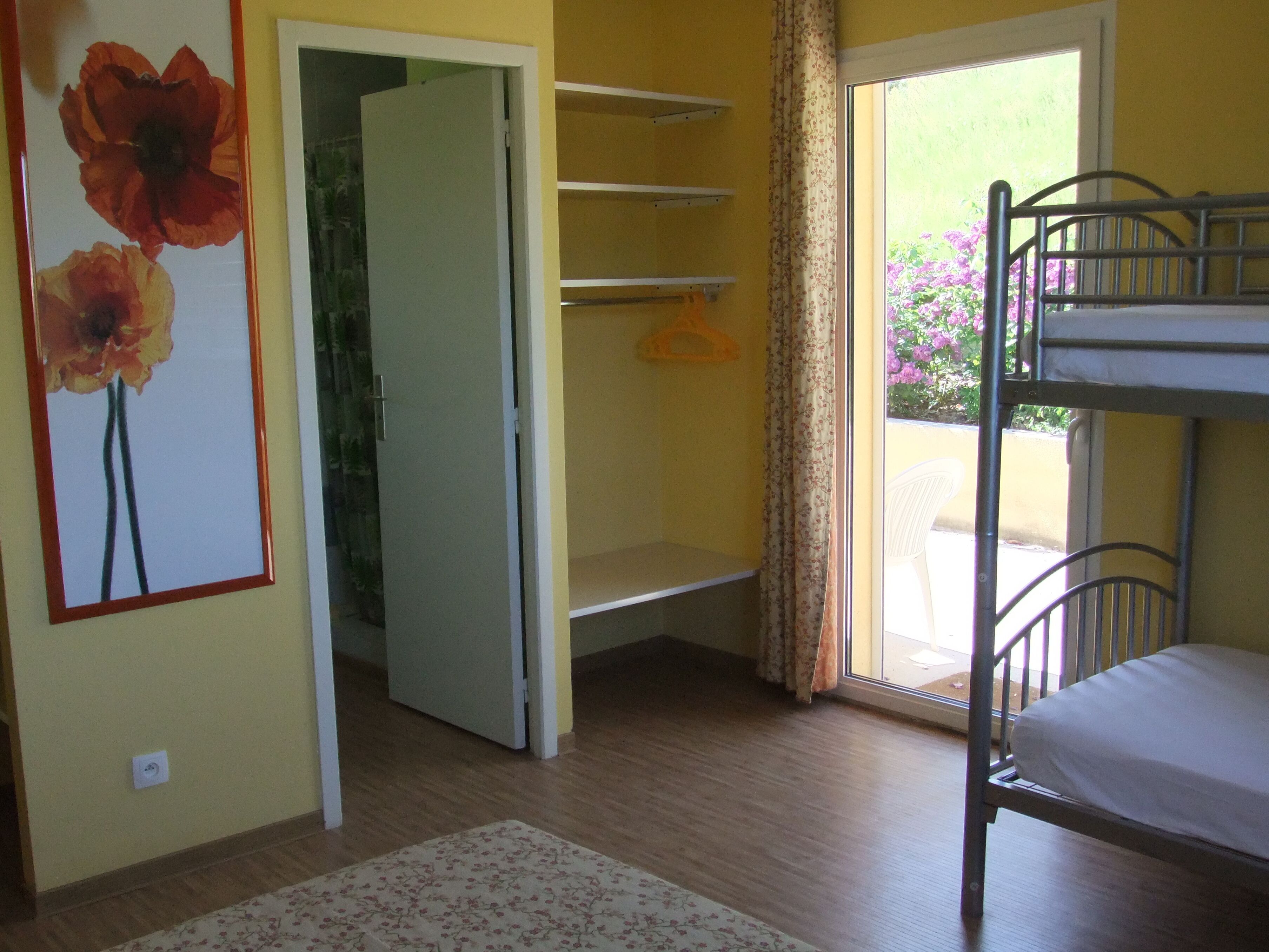 Een kamer met een stapelbed, een deur naar een balkon en een bloemschilderij aan de muur.