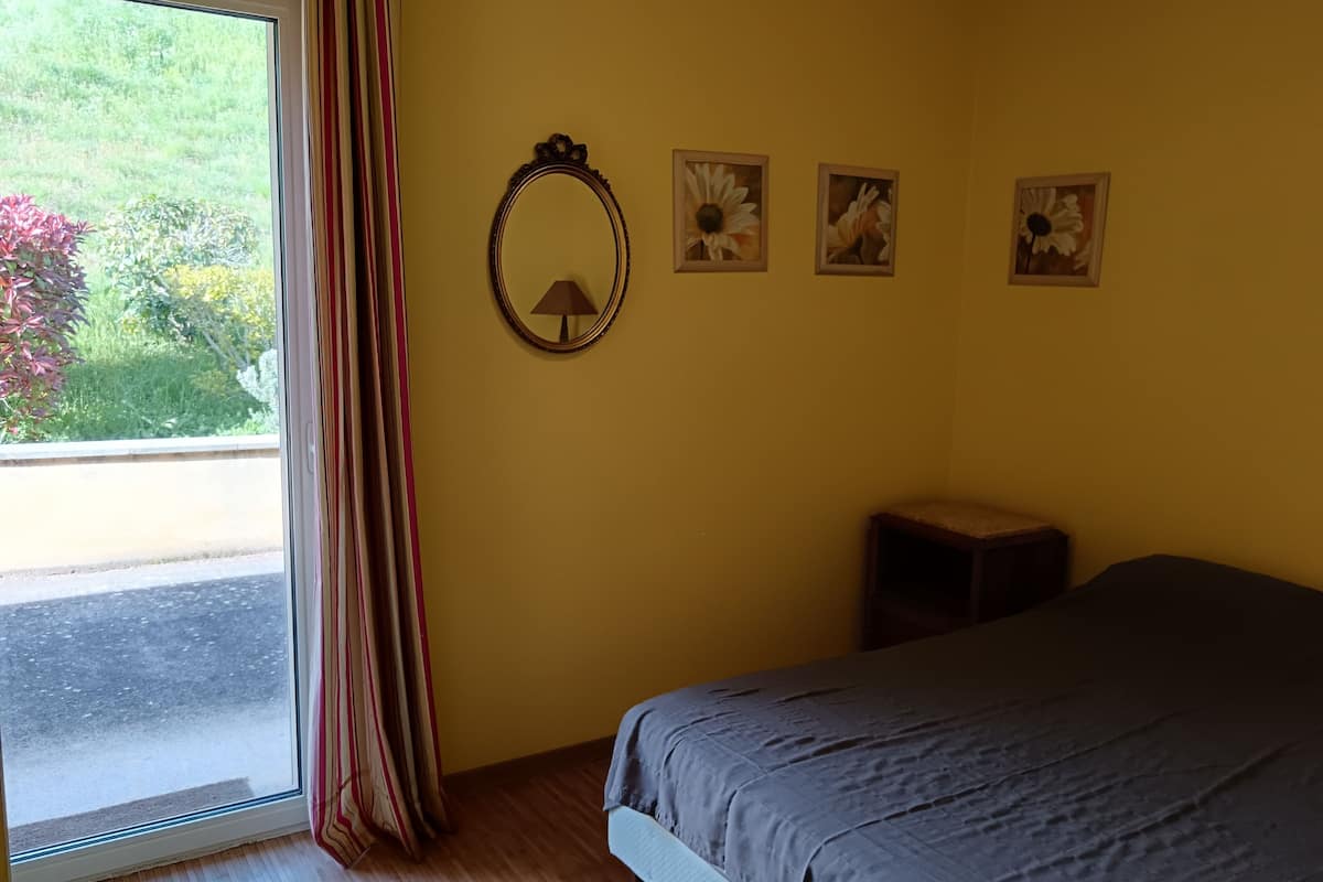 A bedroom with a bed, a window with curtains, a mirror, and three framed pictures on the wall.