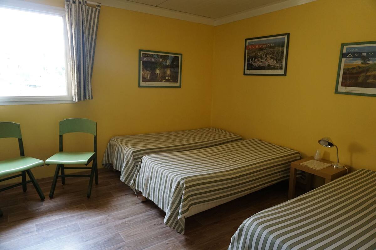 A room with two single beds, a desk, a chair, and a window with curtains.