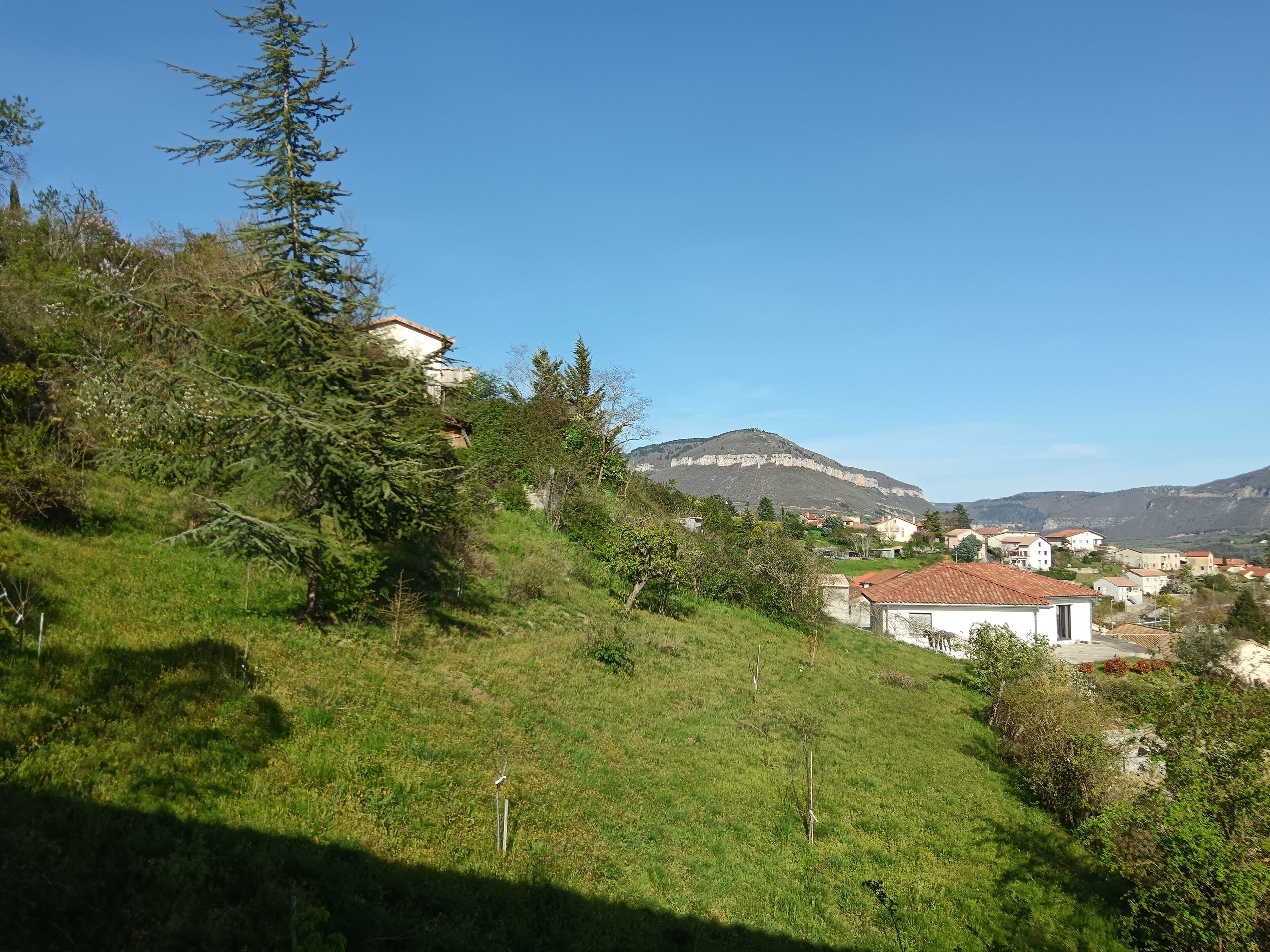 A hillside with houses, a mountain, and a clear sky.