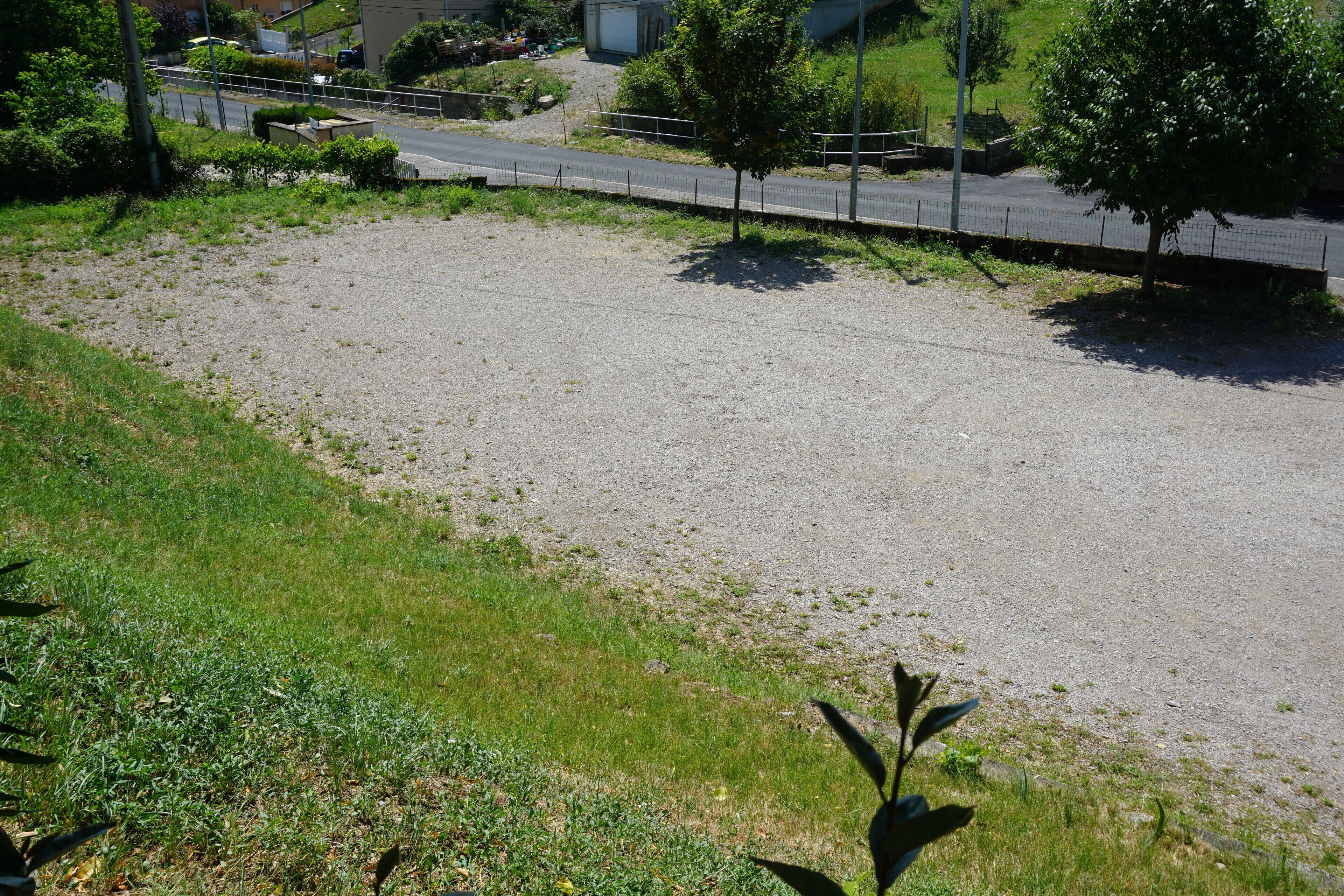 Un parking dont la surface est recouverte de gravier et qui comprend également une zone herbeuse.
