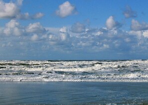 Ein Strand mit Wellen und einem teilweise bewölkten Himmel.