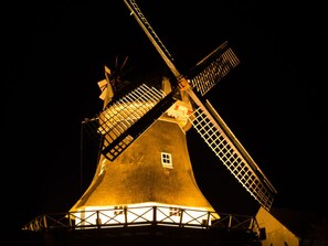 Eine Windmühle bei Nacht mit beleuchteten Flügeln und einem erhellten Fundament.