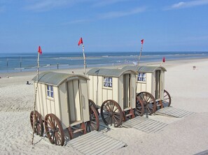 Eine Reihe von Strandhütten auf Rädern mit roten Flaggen, gelegen an einem Sandstrand mit dem Meer im Hintergrund.