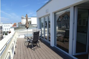 En balkong med ett bord och stolar, en skjutdörr i glas och utsikt över stadsbilden.