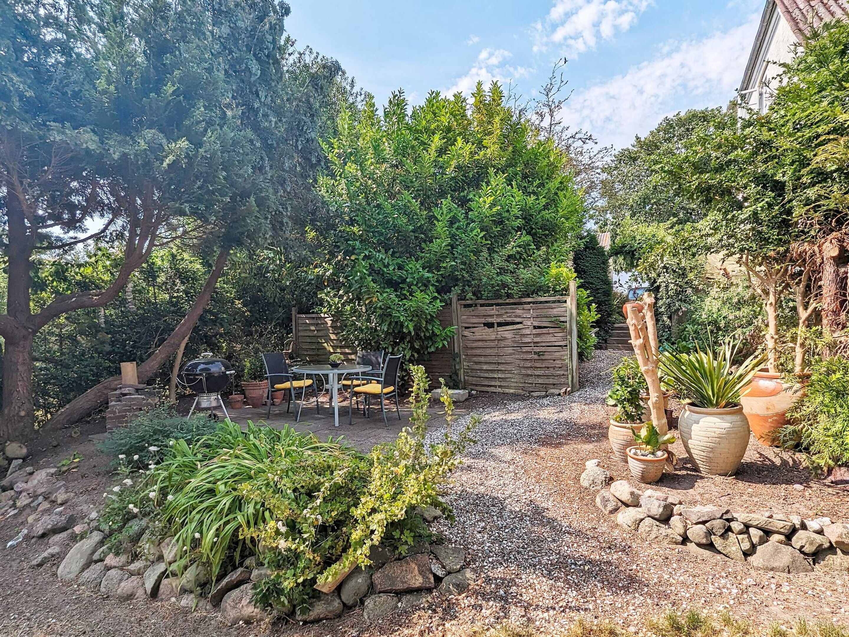 Un jardín con zona de barbacoa, mobiliario exterior y plantas en macetas.