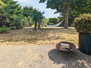 Un'amaca tra gli alberi, un braciere con cataste di legna e un sentiero sterrato.