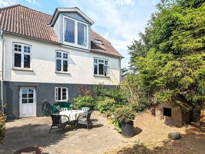 A two-story house with a tiled roof, a balcony, and a garden area with a table and chairs.
