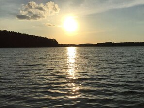 Um lago tranquilo com um pôr do sol refletindo na água, ladeado por uma margem arborizada.