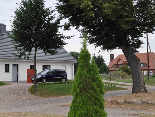 Um bairro residencial com uma casa branca, um carro estacionado e um gramado bem cuidado.