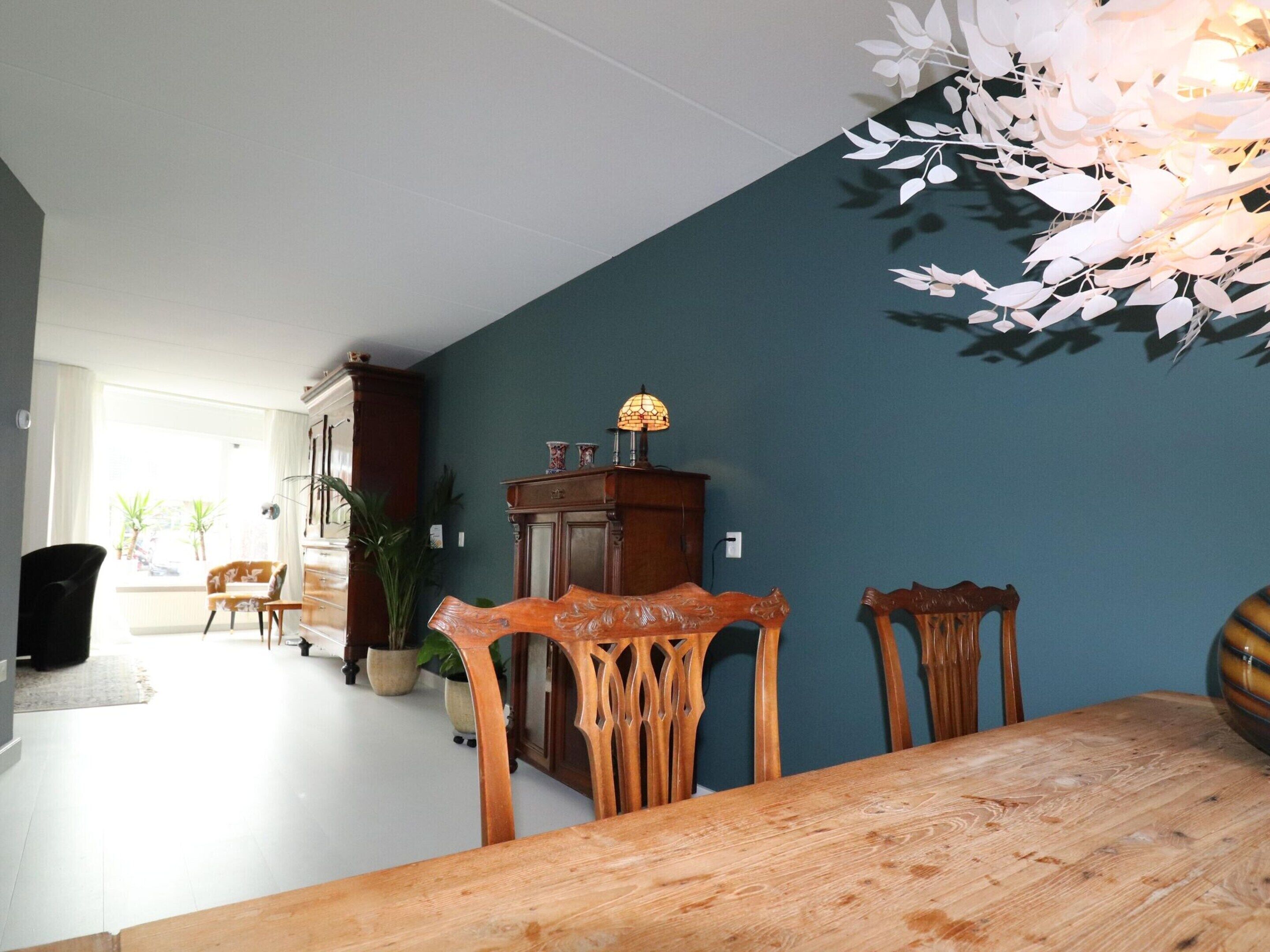 A dining area with a wooden table and chairs, a cabinet with a lamp, and a view of a balcony with plants.