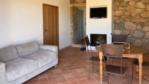 Un saló amb un sofà, una taula de dinar amb cadires, una llar de foc i una paret de pedra.