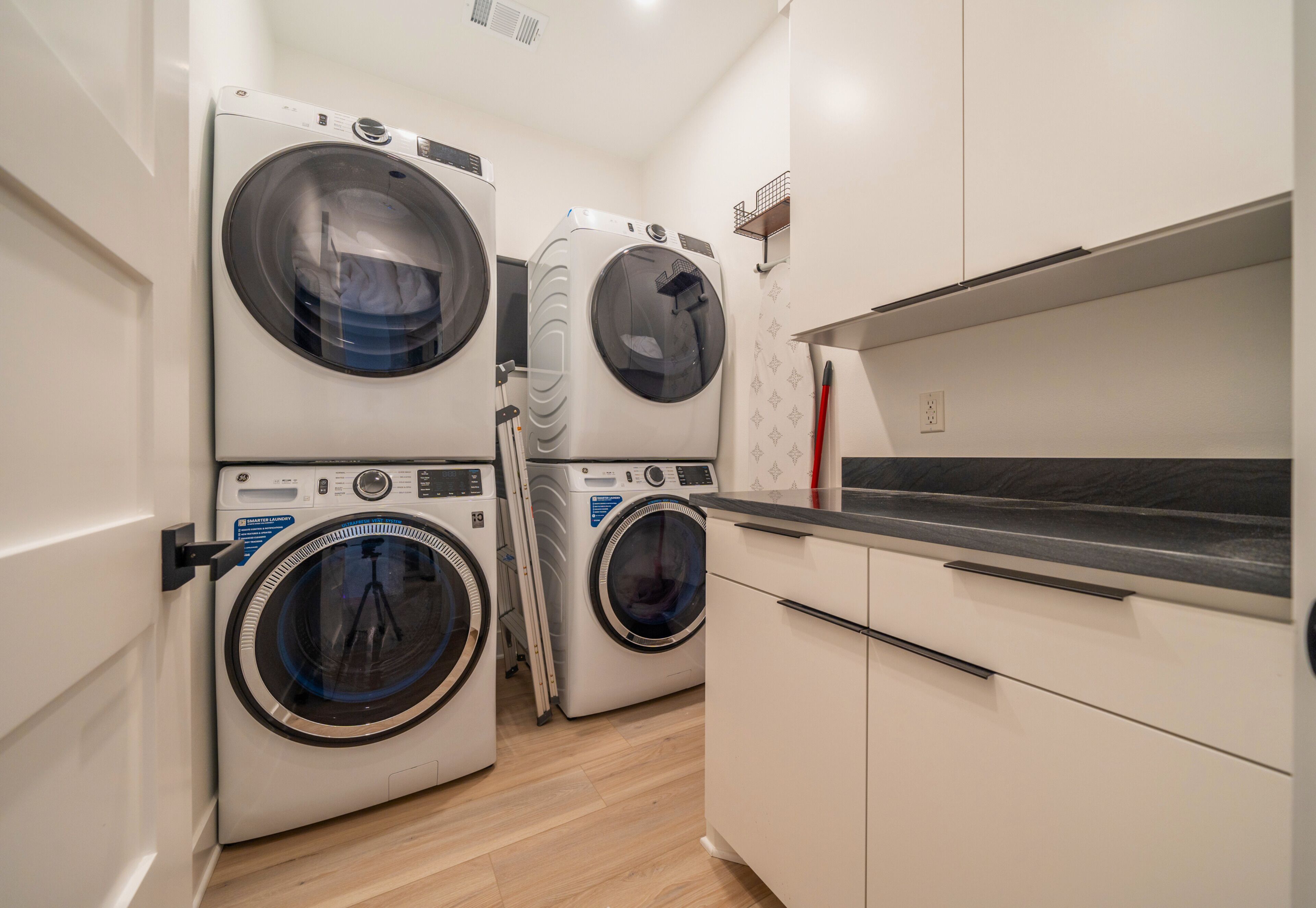 A laundry room with two front-loading washing machines, a countertop, and a cabinet.