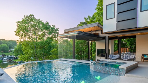 Ein moderner Pool im Freien mit Wasserfall, umgeben von üppiger Vegetation und einem zeitgemäßen Haus.