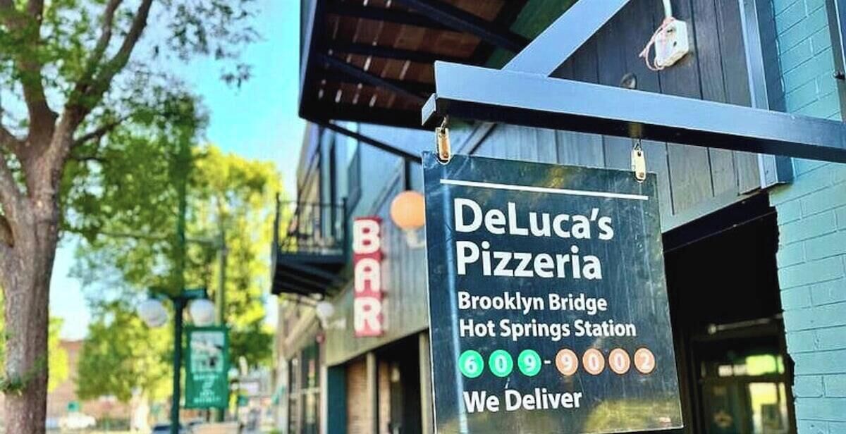 A sign for DeLuca's Pizzeria with a delivery service, located at Brooklyn Bridge Hot Springs Station.