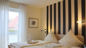 A hotel room with two beds, a window with white curtains, a wall-mounted light fixture, and a framed picture on the wall. - "landlust" Modern Retreat (Kellenhusen)
