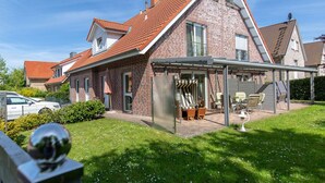 A two-story house with a red-tiled roof, a covered patio area with outdoor furniture, and a well-maintained lawn. - "landlust" Modern Retreat (Kellenhusen)