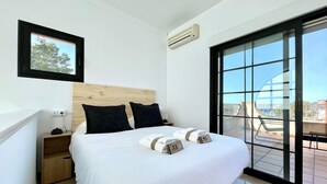 Una habitación de hotel moderna con una cama grande, un cabecero de madera, una mesita de noche, un enchufe y un ventanal con vistas a la ciudad.