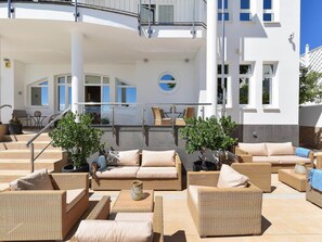 A sunlit outdoor seating area with wicker furniture, a circular window, and a view of a building with balconies. - Belvilla by OYO Villa Doramas 12 pax (Mogan)