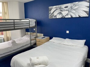 Habitación de hotel con literas, una cama individual, una mesita de noche, un control remoto y un cuadro con motivos florales en la pared.