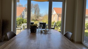 A dining area with a large wooden table, black chairs, a black pendant light, and a vase with flowers. - Northern Light House (Kosel)