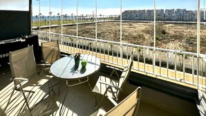 Un balcón con mesa y sillas, un televisor y vistas a un paisaje urbano y un campo seco.