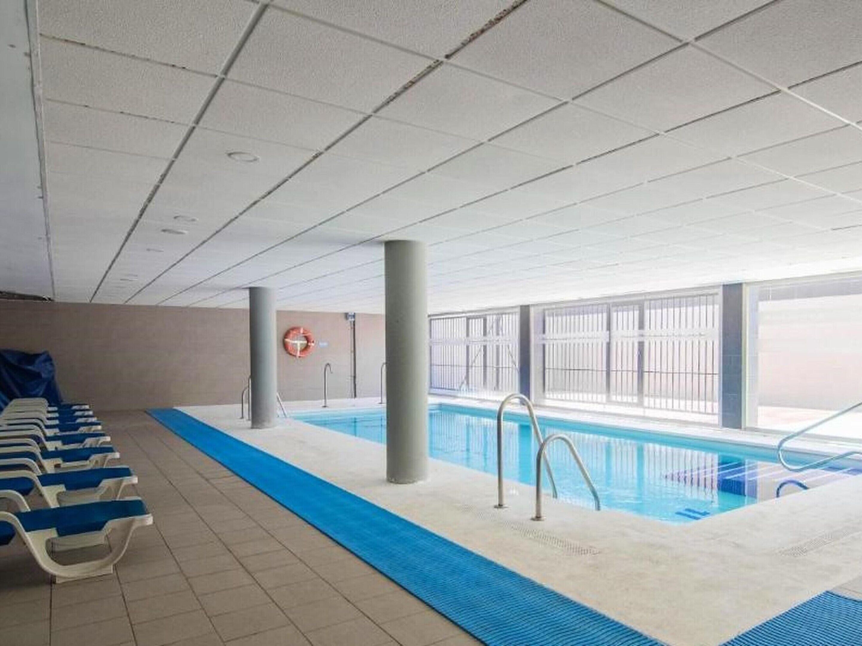 Una piscina interior amb aigua blava, un separador de línies blau i seients ganduls blancs al costat de la piscina.