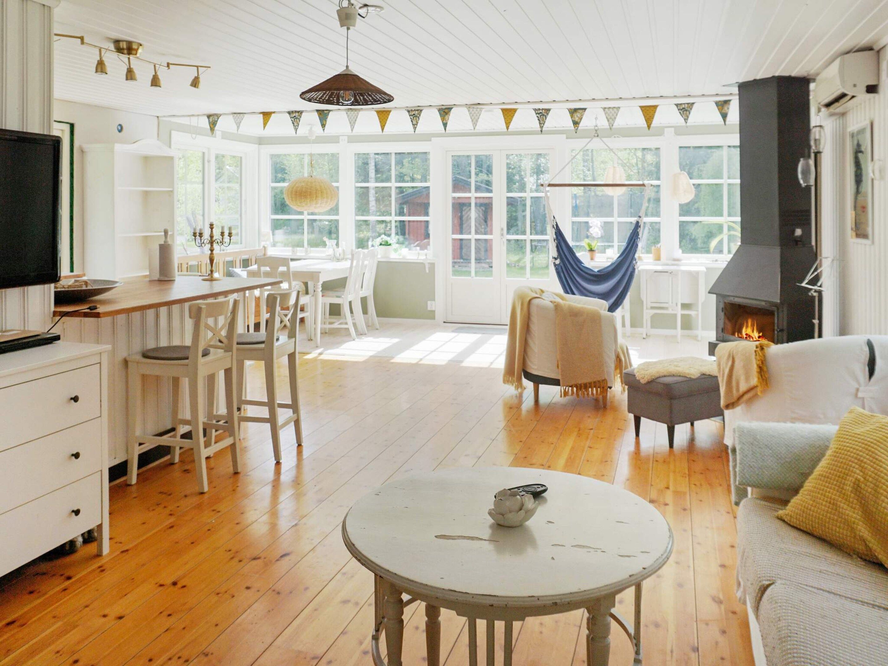 Un salón comedor amplio con chimenea, suelo de madera y mobiliario blanco.