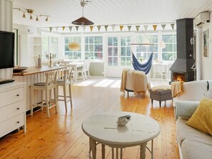 A spacious living room with a fireplace, wooden flooring, and a dining area with white furniture. - 4 Star Holiday Home in Grisslehamn (Grisslehamn)