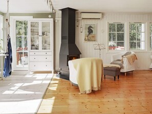 A room with a fireplace, a sofa, a cabinet, and large windows. - 4 Star Holiday Home in Grisslehamn (Grisslehamn)