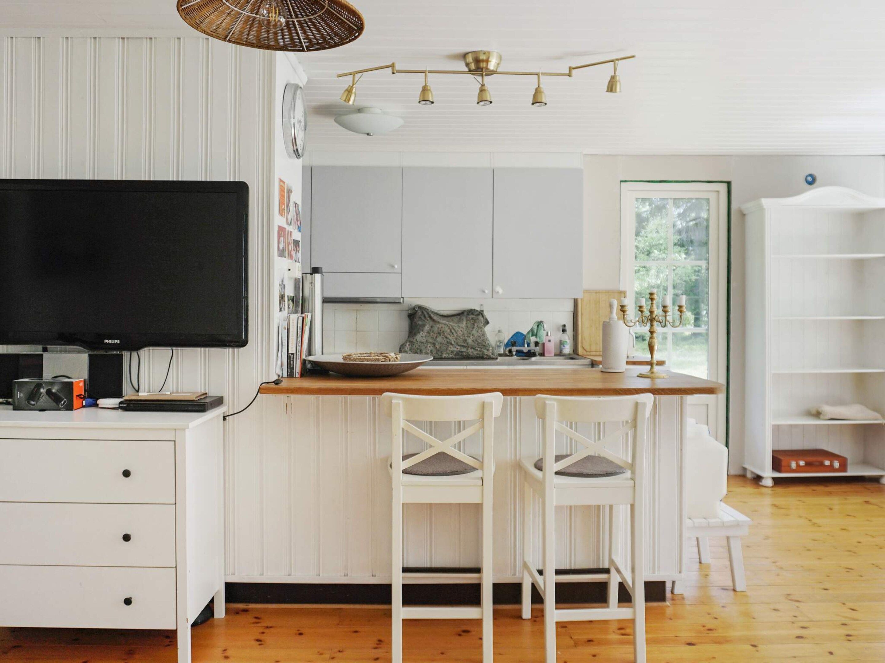 A modern kitchen with white cabinetry, a wooden island, and a flat-screen TV.