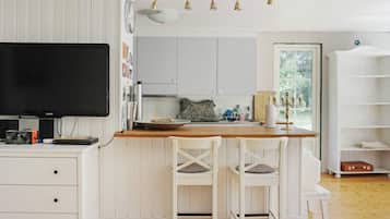 A modern kitchen with white cabinetry, a wooden island, and a flat-screen TV.