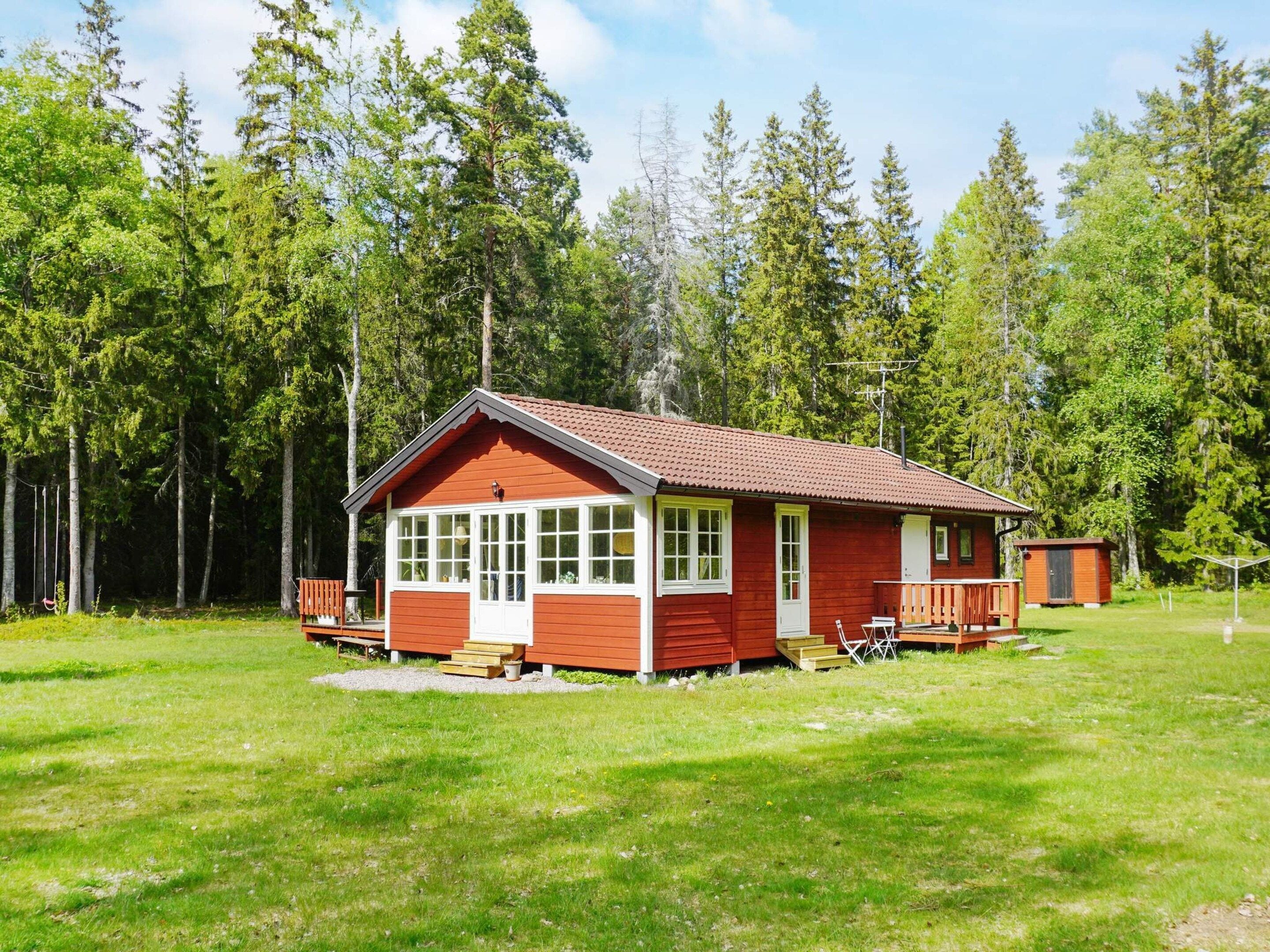 A red wooden cabin with a porch, large windows, and a small attached shed.