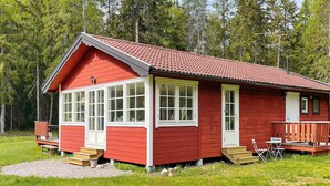 A red cabin with white trim, large windows, and a porch with chairs. - 4 Star Holiday Home in Grisslehamn (Grisslehamn)